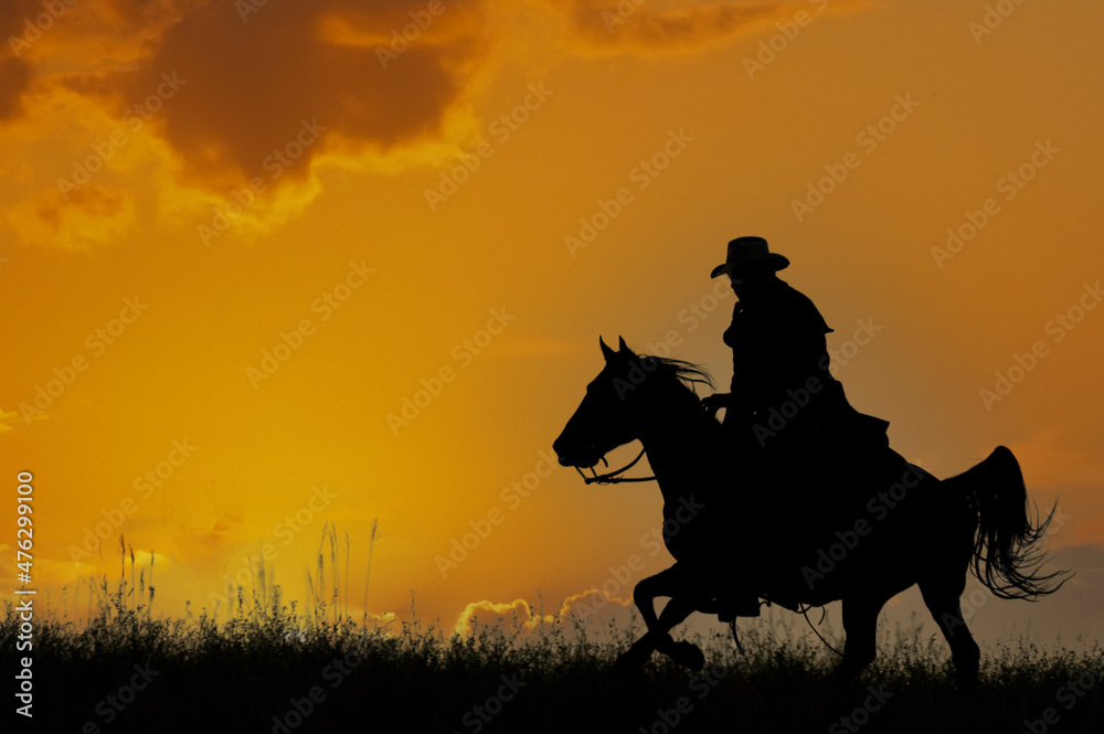 Cowboy galloping across hill against dawn sky