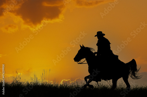 Cowboy galloping across hill against dawn sky