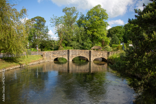 Beautiful small bridge over calm water and green trees in summer at Arlington, UK