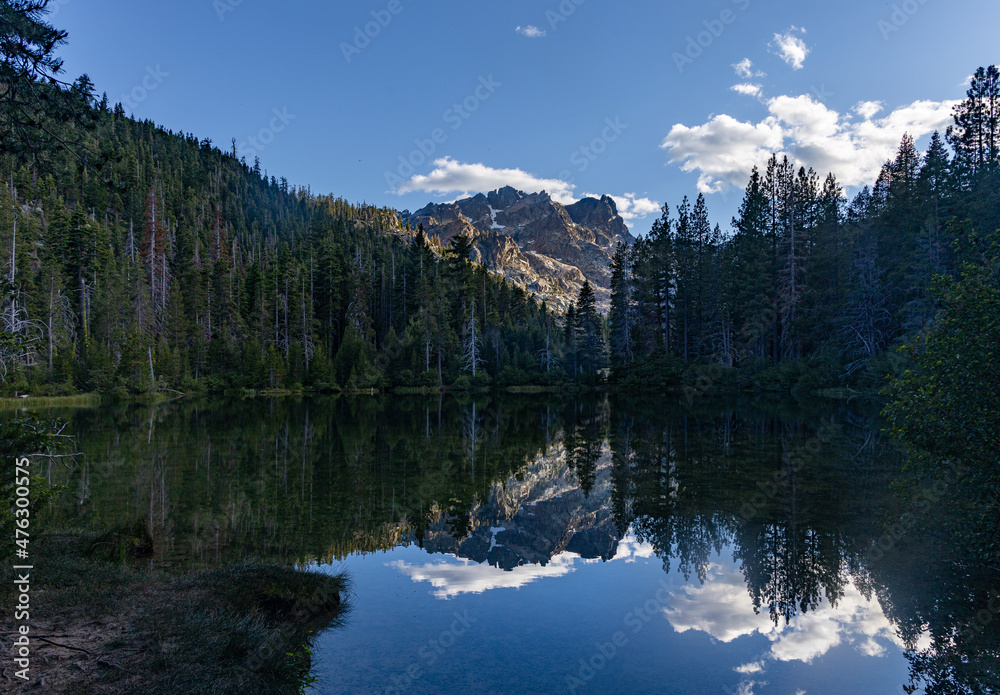 High elevation alpine lake in California reflecting the mountains trees and blue sky with clouds.