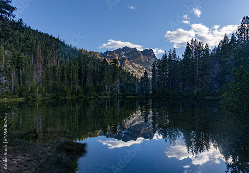 High elevation alpine lake in California reflecting the mountains trees and blue sky with clouds. © Donald Blodger