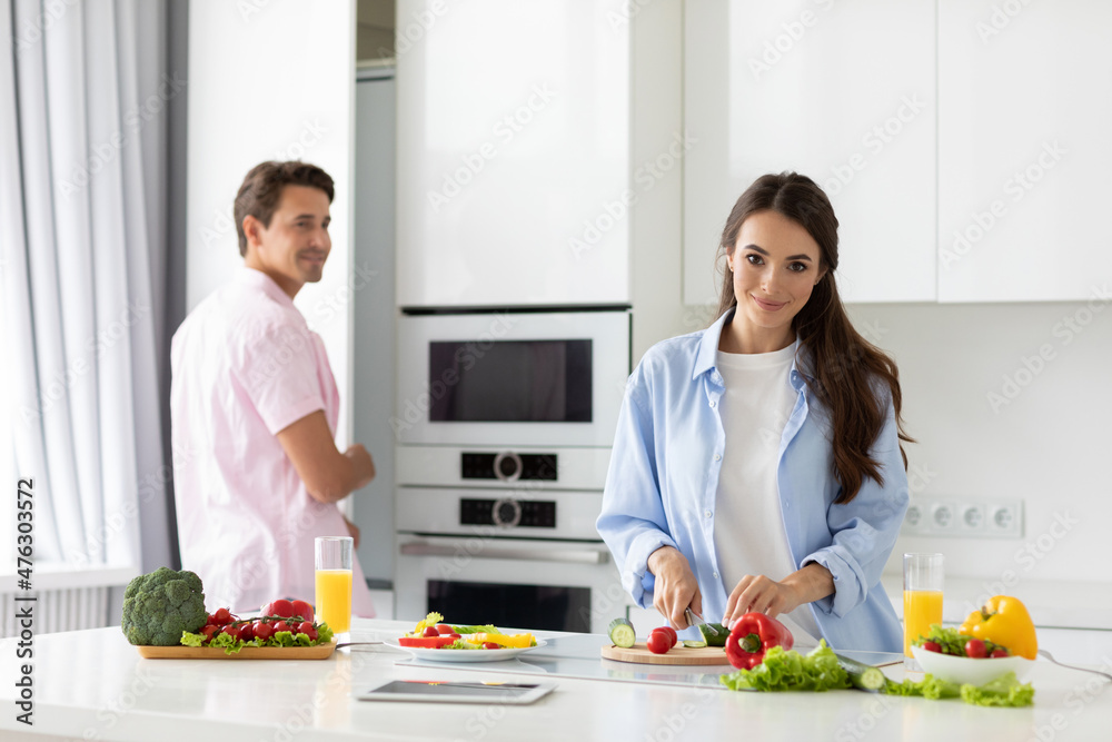 Joyful young couple in kitchen at home preparing vegetable salad.