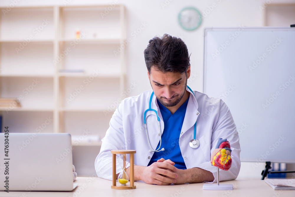 Young male doctor cardiologist in time management concept Young male doctor cardiologist in time management concept