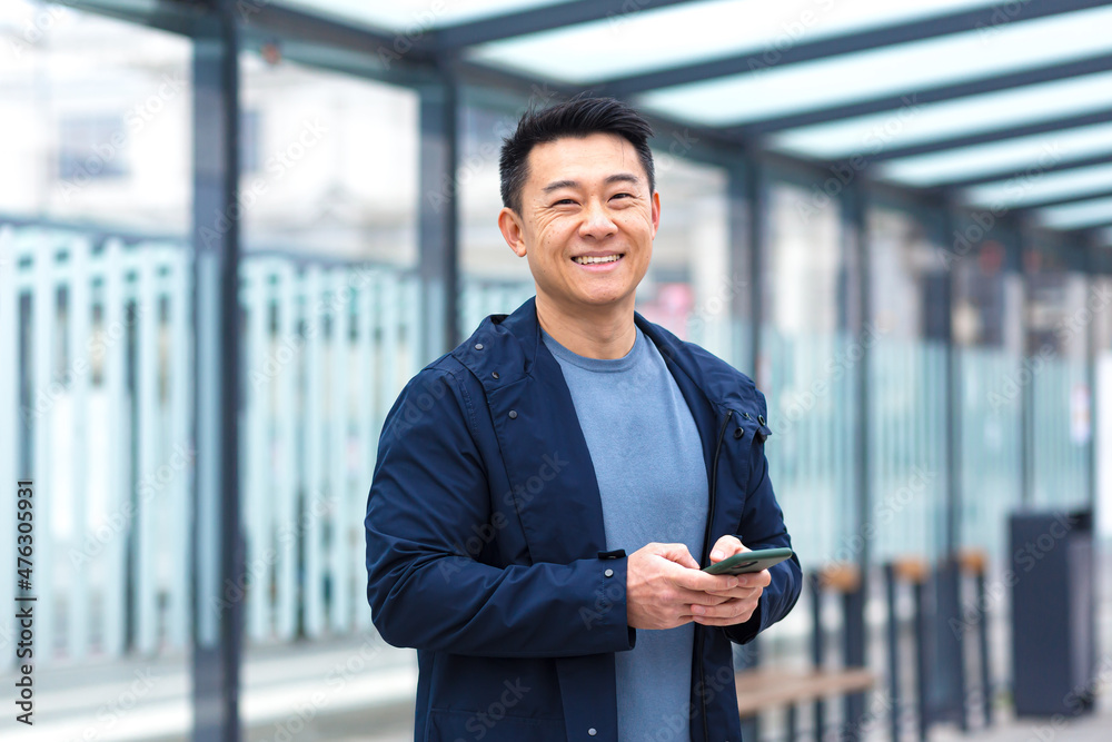 Cheerful and happy asian using phone smiling and looking at camera, near airport, businessman on tourist trip Cheerful and happy asian using phone smiling and looking at camera, near airport, businessman on tourist trip