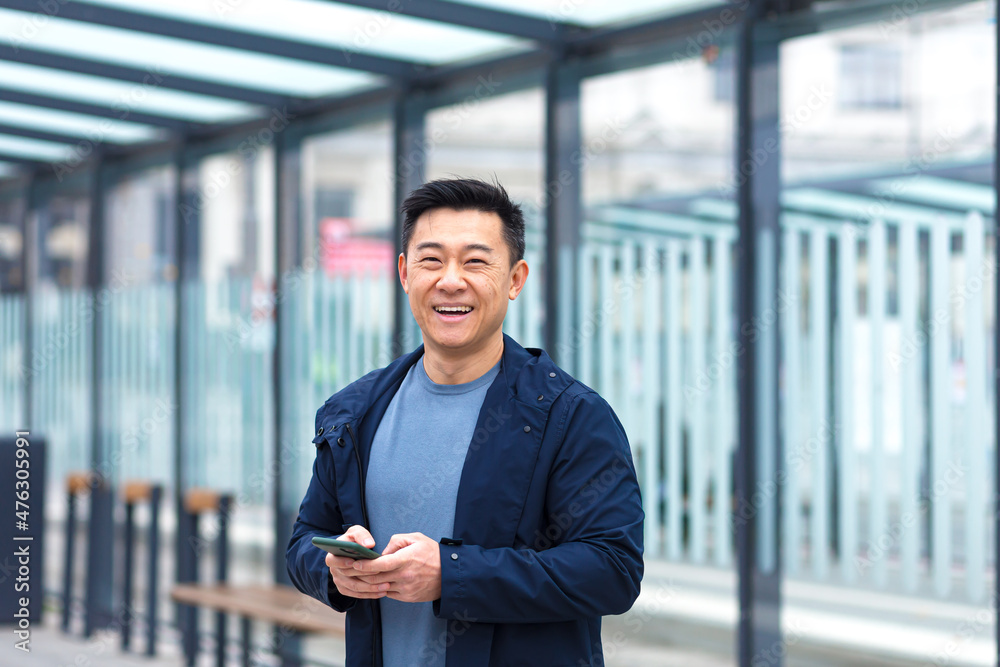 Cheerful and happy asian using phone smiling and looking at camera, near airport, businessman on tourist trip Cheerful and happy asian using phone smiling and looking at camera, near airport, businessman on tourist trip