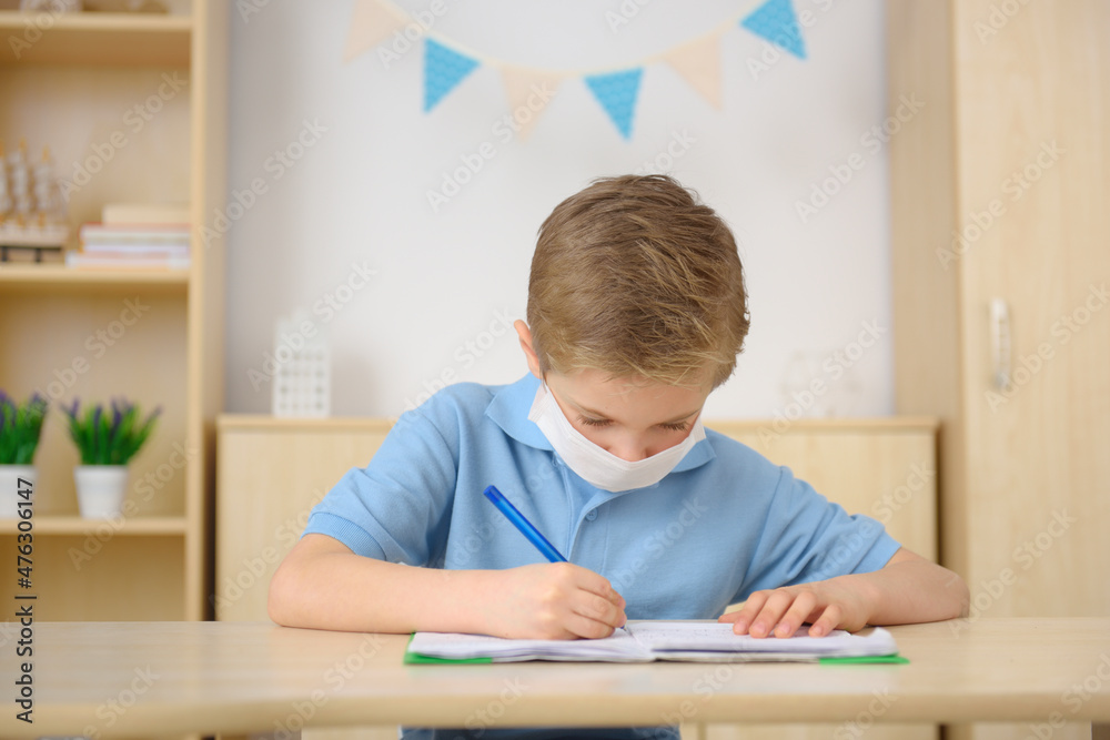 A little boy in a medical mask is learning at home. A little boy in a medical mask is learning at home.