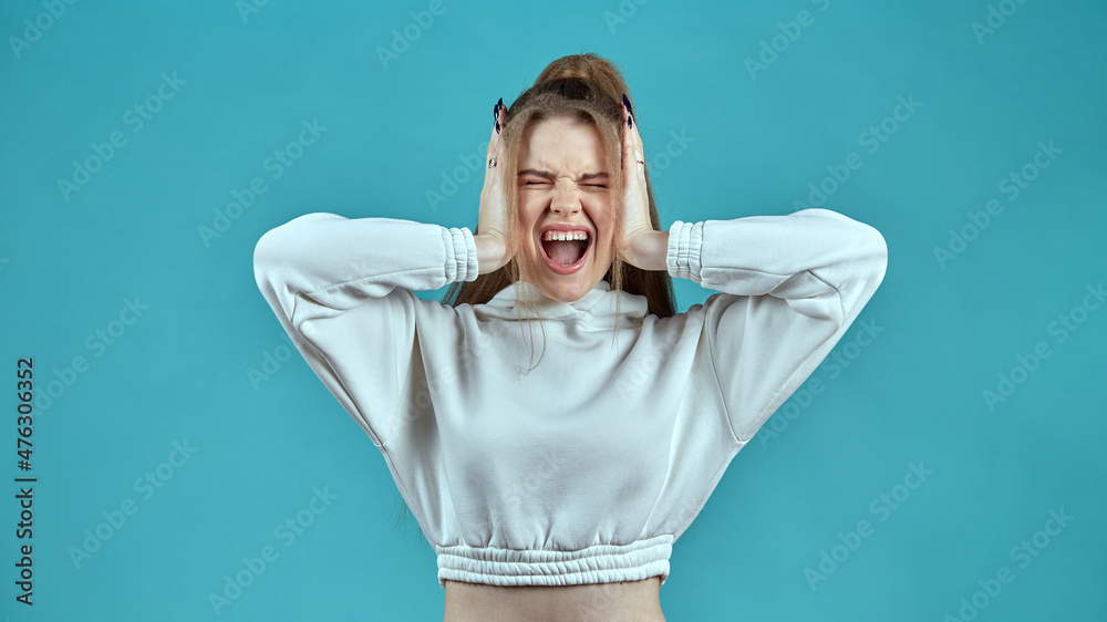 the girl screams covering her ears with her hands standing on a blue background the girl screams covering her ears with her hands standing on a blue background