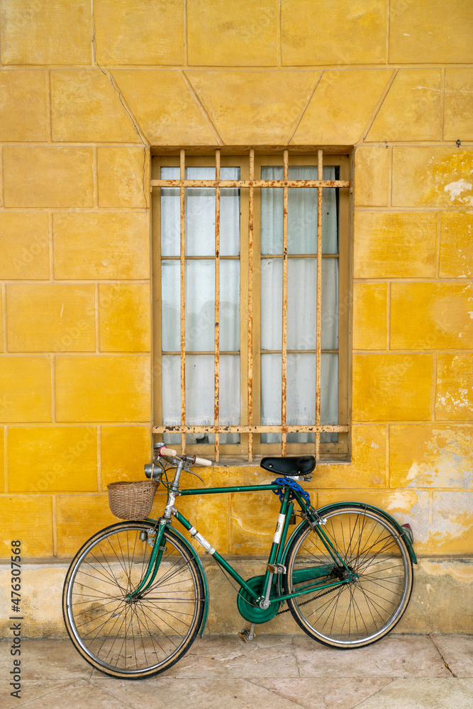 Old green bicycle leaning against yellow wall of rural Italian house