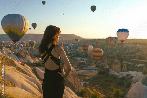 Fototapeta Woman watching the sunrise and hot air balloons taking off over valley in Cappad