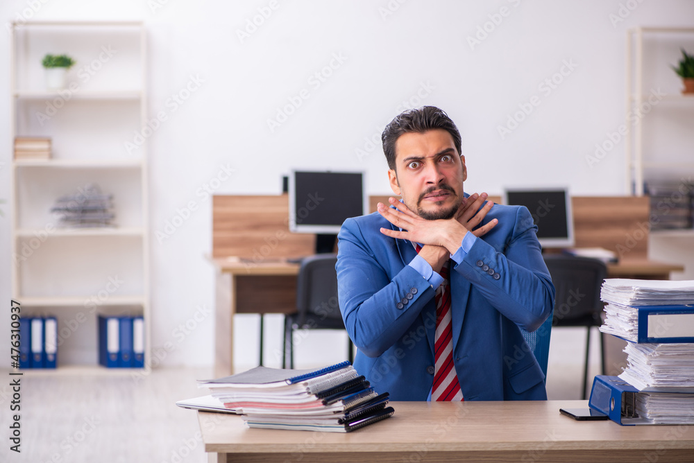 Young male employee unhappy with excessive work at workplace Young male employee unhappy with excessive work at workplace