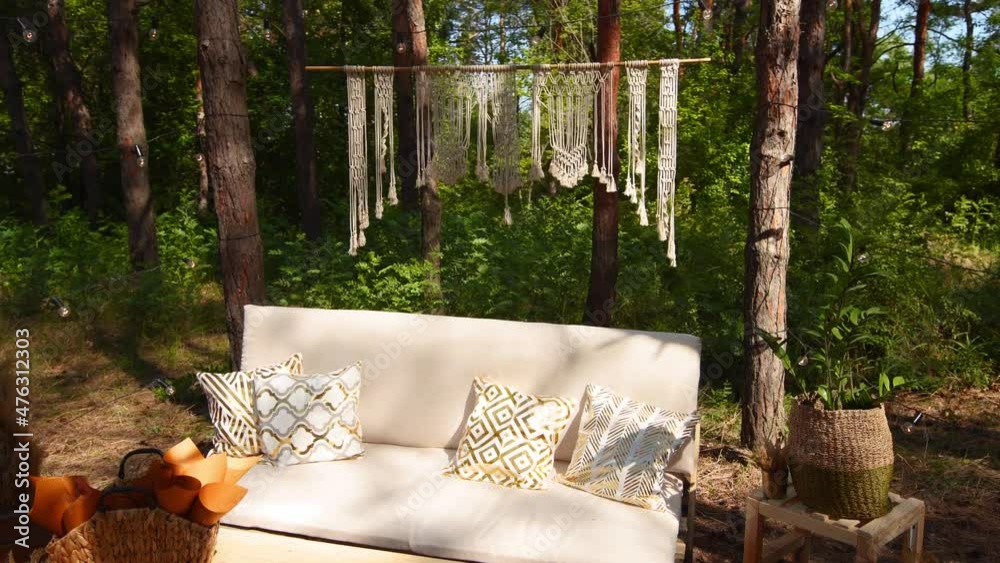 Lounge photo zone with diy sofa and table of cargo pallets in boho style on outdoor wedding ceremony venue in pine forest. Bohemian decor.