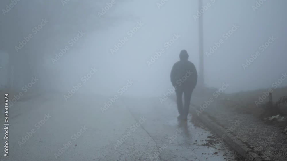 Lonely man walking in mystery fog on dirty road