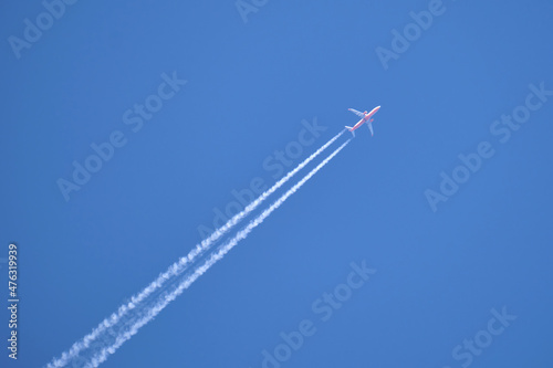 Bilde på lerret Distant passenger jet plane flying on high altitude on clear blue sky leaving white smoke trace of contrail behind