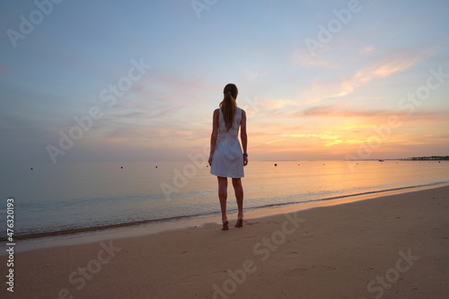 Lonely young woman standing on sandy beach by seaside enjoying warm tropical evening © bilanol