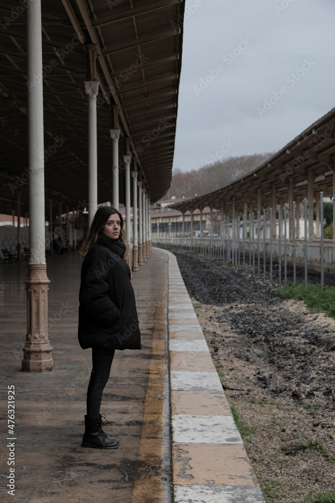 A girl is waiting in empty train station in fall winter season. Vertical photo. Separation, break up, longing and missing concept photo. Loneliness.