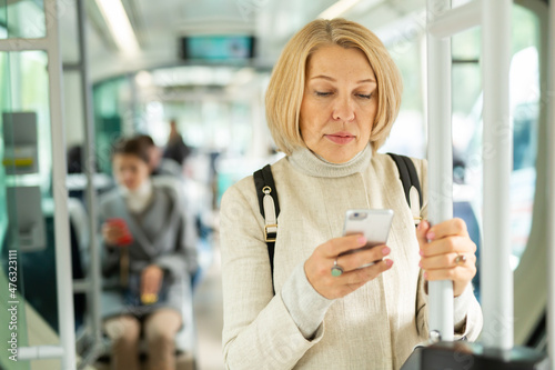 Portrait of focused mature woman absorbed in her smartphone on way to work in modern streetcar in autumn day