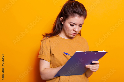 Young woman taking notes on textbook papers with pen in studio. Concentrated person writing on notebook files and signing documents and paperwork about project on notepad clipboard.