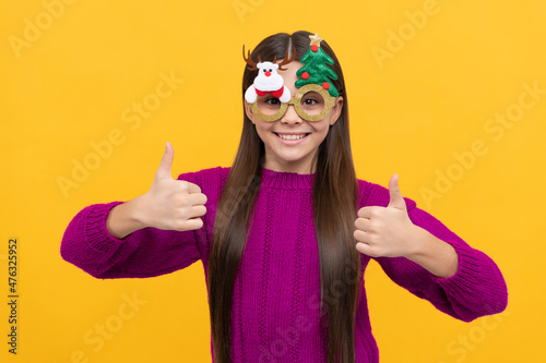 happy child in party glasses showing thumb up on yellow background, christmas