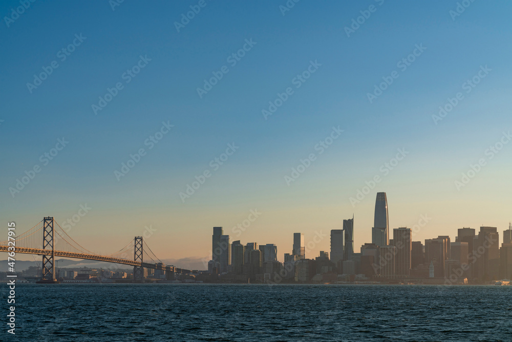 A picturesque view of The Bay Bridge and San Francisco Skyline Panorama at sunset golden hour from Treasure Island, California, United States. Cityscape with mist and foggy air.