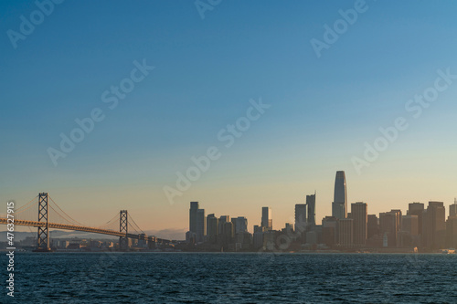 A picturesque view of The Bay Bridge and San Francisco Skyline Panorama at sunset golden hour from Treasure Island, California, United States. Cityscape with mist and foggy air.