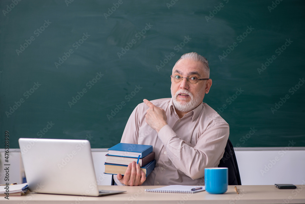 Old male teacher in front of blackboard Old male teacher in front of blackboard
