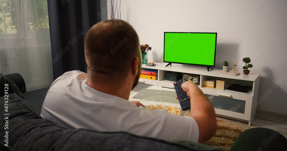 Man Watching Green Chroma Key Tv Screen and Changing Channels with Remote Control several times. Male sitting on the couch in the living room in the evening Man Watching Green Chroma Key Tv Screen and Changing Channels with Remote Control several times. Male sitting on the couch in the living room in the evening