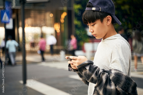Photography teenage asian boy using mobile phone outdoors on street