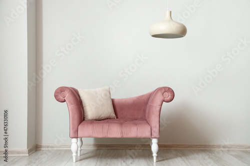 Pink armchair with pillow and hanging lamp near light wall © Pixel-Shot