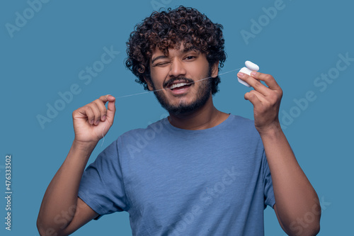 Tablou pe pânză Bearded curly-haired mustached man flossing his teeth