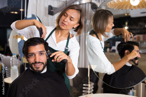 female professional shaving cheerful male's hair in hairdressing salon