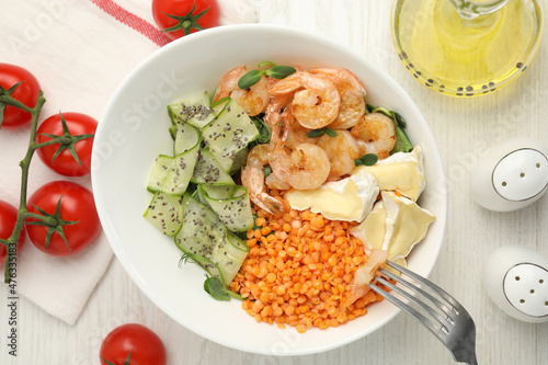Delicious lentil bowl with shrimps, soft cheese and cucumber on white wooden table, flat lay