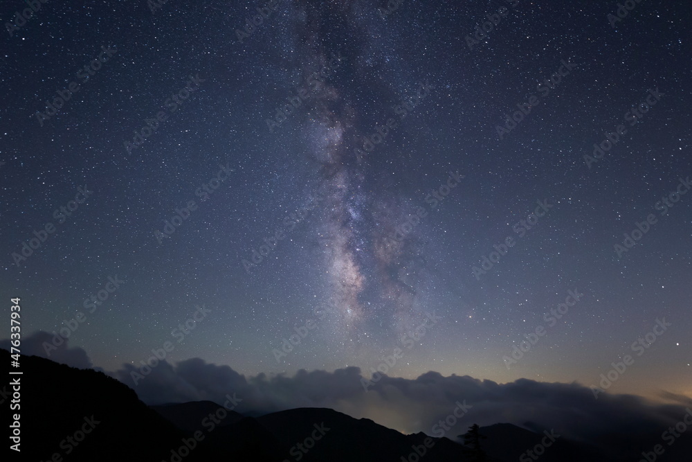 山並みを覆う雲の上に輝く星々と天の川