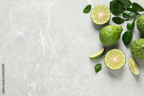 Fresh ripe bergamot fruits with green leaves on light grey marble table, flat lay. Space for text photo