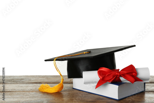 Graduation hat, book and diploma on wooden table against white background