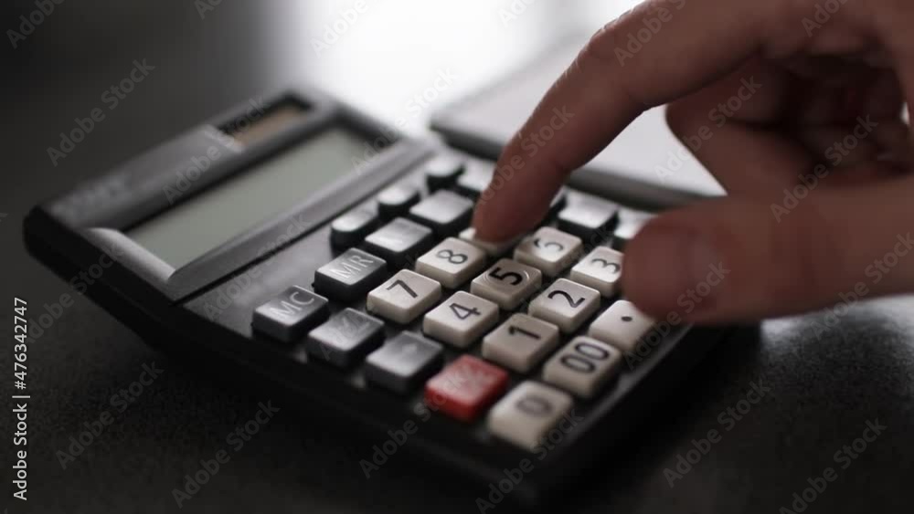 Close up of a hand typing on calculator and using notepad Close up of a hand typing on calculator and using notepad