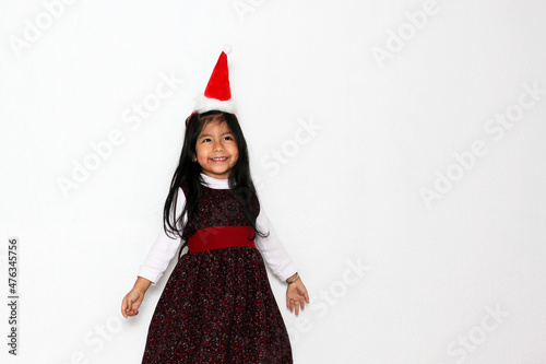 Little brunette Latina girl in red party dress and Christmas hat excited and happy for the arrival of December and celebrate Christmas and New Years 