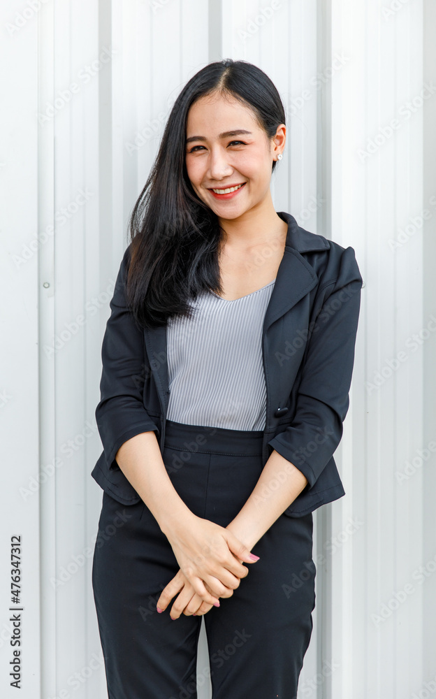 Portrait shot of Asian young happy cheerful millennial long black hair successful professional businesswoman female model in formal office working suit stand smiling look at camera on wall background Portrait shot of Asian young happy cheerful millennial long black hair successful professional businesswoman female model in formal office working suit stand smiling look at camera on wall background