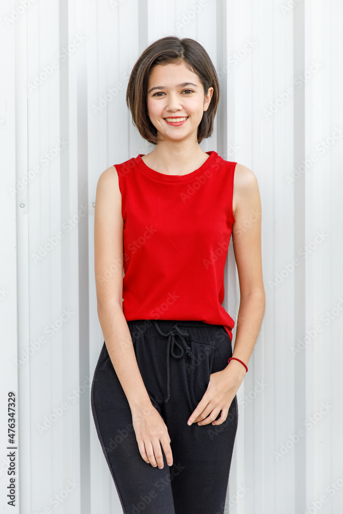 Portrait shot of Asian young happy cheerful millennial short hair teenager female model in red sleeveless shirt and black sweatpants standing crossed arms smiling look at camera on wall background Portrait shot of Asian young happy cheerful millennial short hair teenager female model in red sleeveless shirt and black sweatpants standing crossed arms smiling look at camera on wall background