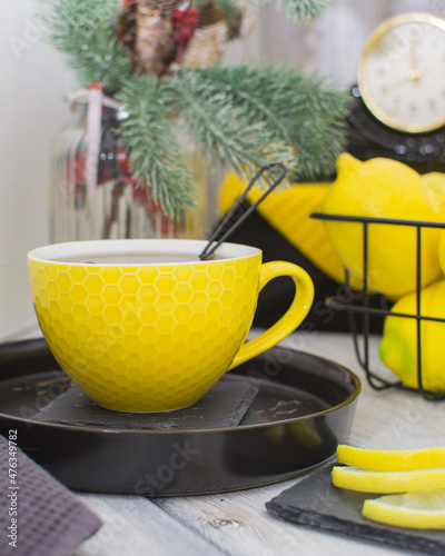 A yellow glass of tea on a black porcelain tray. In the background is a black metal basket with lemons.