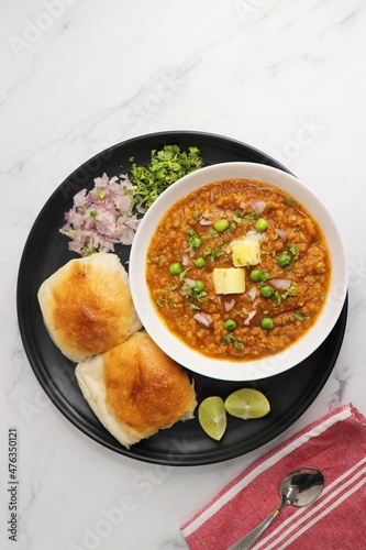Indian Mumbai Street style Pav Bhaji, garnished with peas, raw onions, coriander, and Butter. Spicy thick curry made of out mixed vegetables served with pav over white background with copy space.