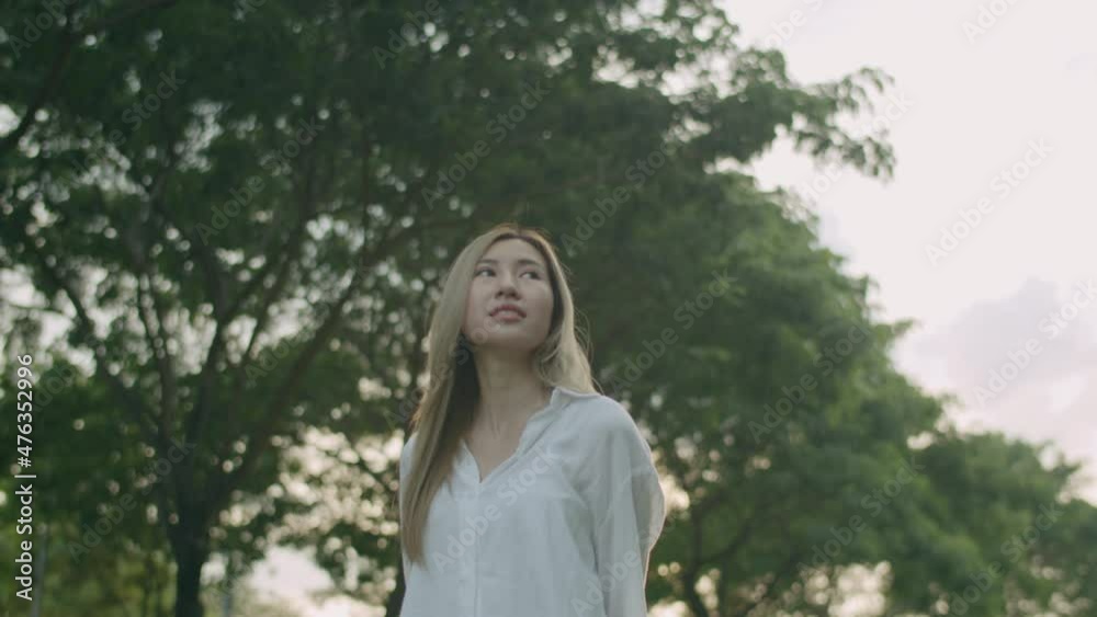 Beautiful young Asian woman looking around her enjoying the breeze in the public park during a beautiful sunset. Beautiful young Asian woman looking around her enjoying the breeze in the public park during a beautiful sunset.