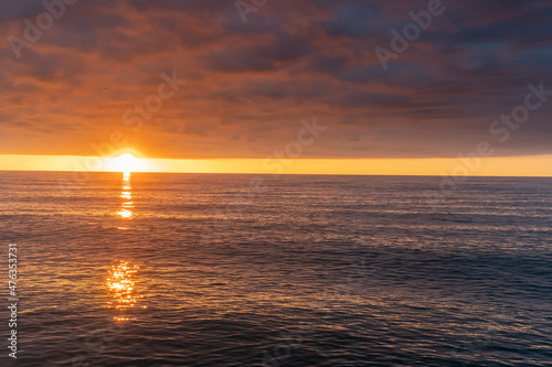 Bright orange sunset over the sea. Reflection by glare of sunlight in the water. Beautiful cloudy sky