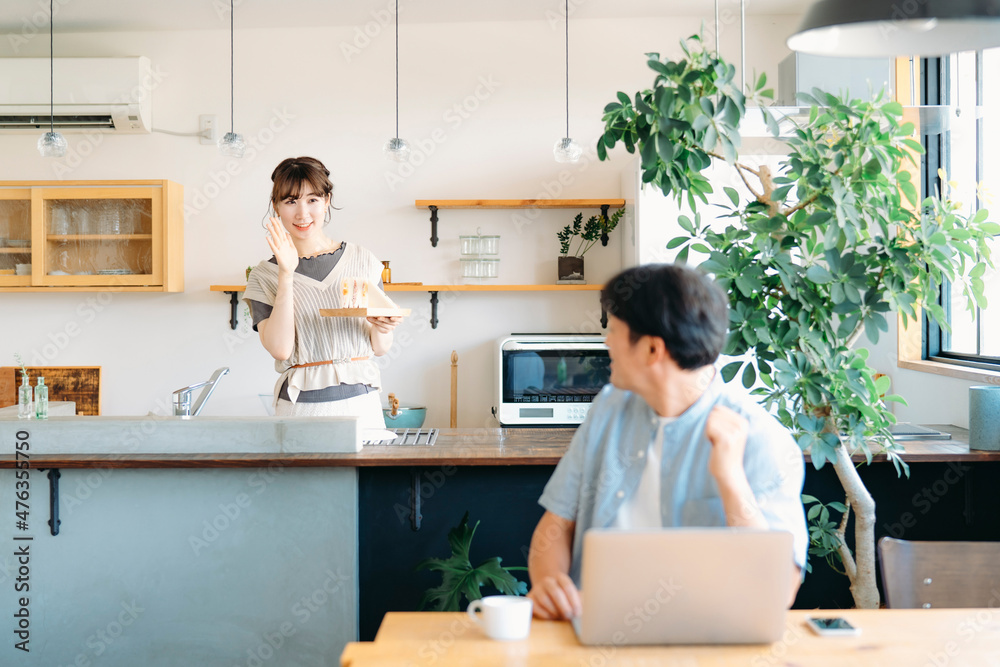 テレワークする男性とキッチンにいる女性
テレワークする男性とキッチンにいる女性