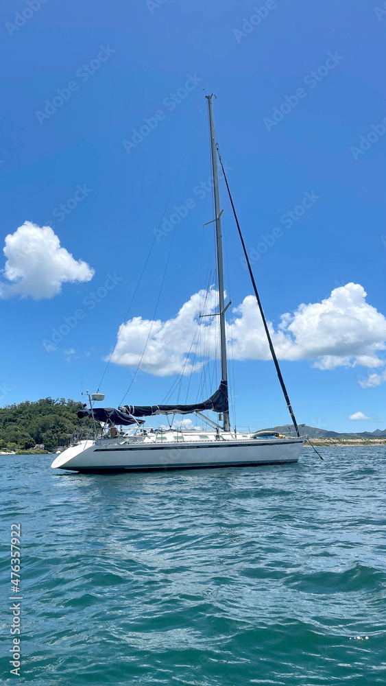 Naklejka premium Vertical recreational sailing boat on ocean with mountain, blue sky and clouds in Hong Kong