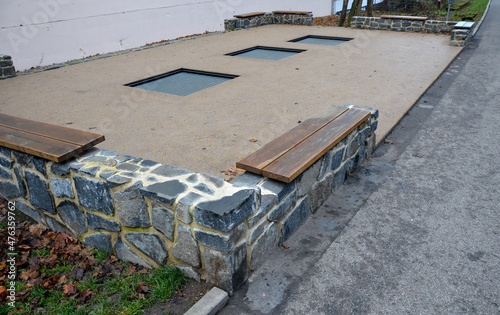 in the courtyard of school playground, three trampoline jumping mats are sunk below level of a special rubber surface. around are wooden benches attached to the stone walls of a picturesque backyard photo