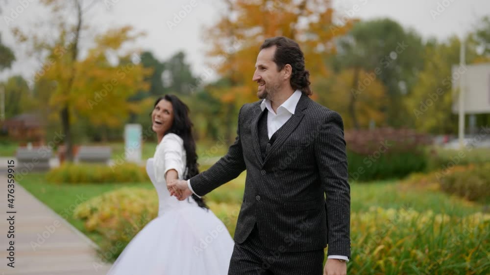 the bride and groom hold hands, laugh and dance in the autumn park. the middle plan. the camera is moving the bride and groom hold hands, laugh and dance in the autumn park. the middle plan. the camera is moving