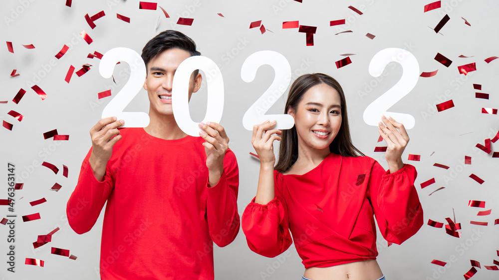 Lovely Asian couple smiling and showing number 2022 for new year concept on light gray studio background with confetti