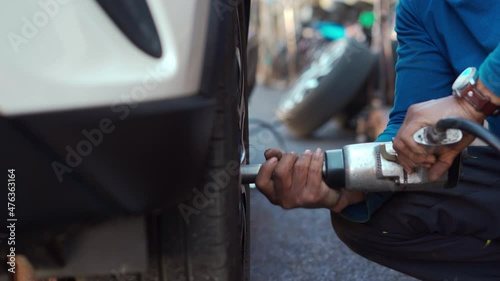 mechanic man using an electric drill to loosen the bolts of vehicle wheel for changing a car tire
