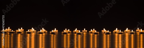 Burning orange candles on panoramic black background. Candlelights reflected on the table. Mourn and Christmas concept.