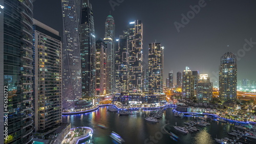 Dubai marina tallest skyscrapers and yachts in harbor aerial night timelapse.